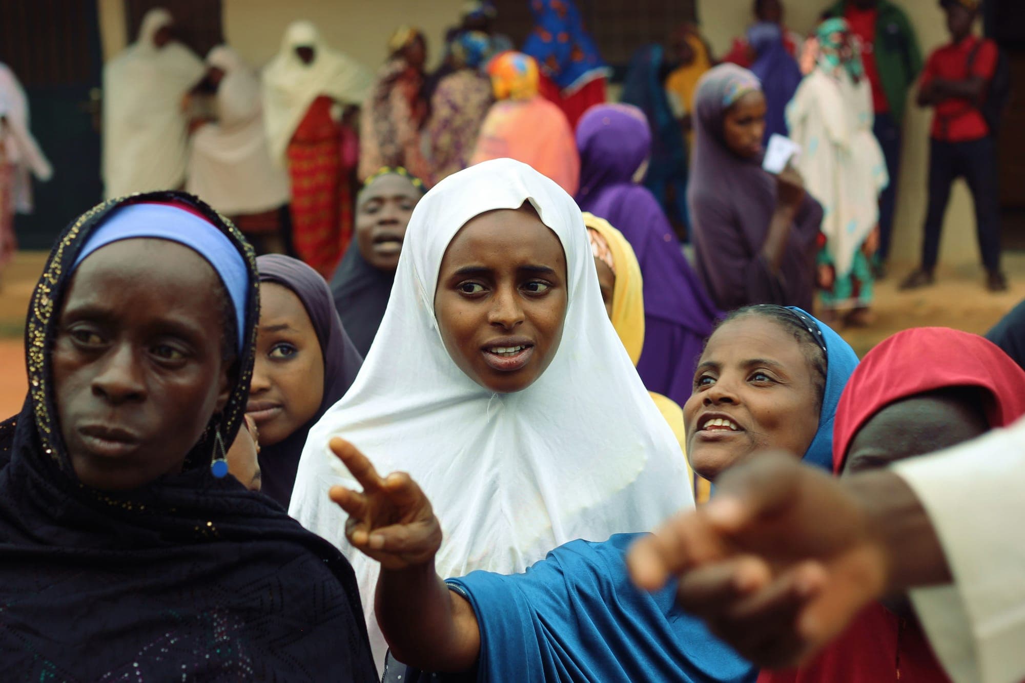 Citizens waiting at a polling station, a voter card visible in the crowd
