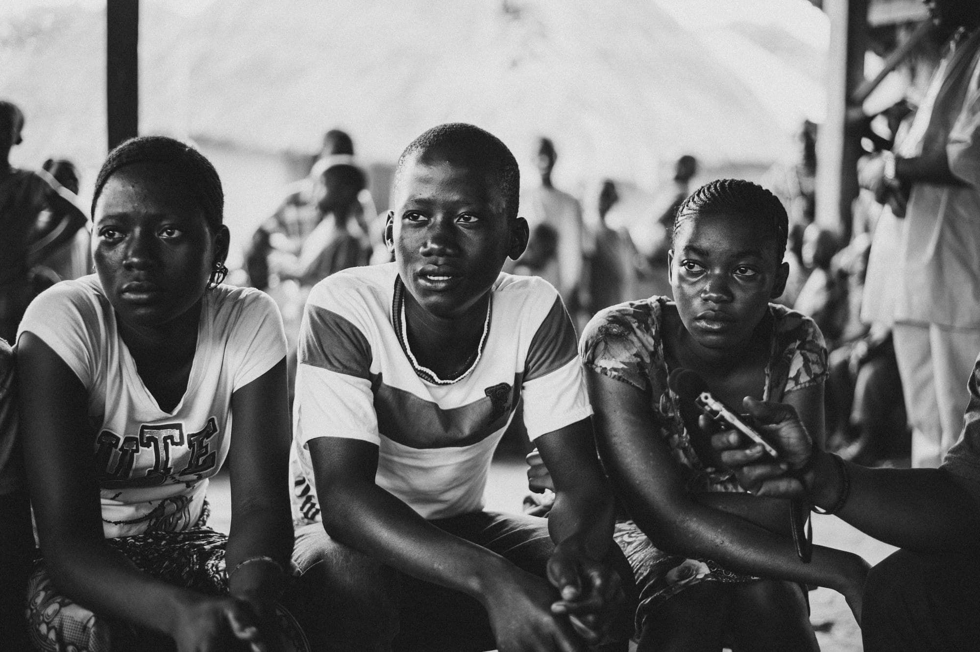 Black-and-white portrait of three young people, one holding a phone