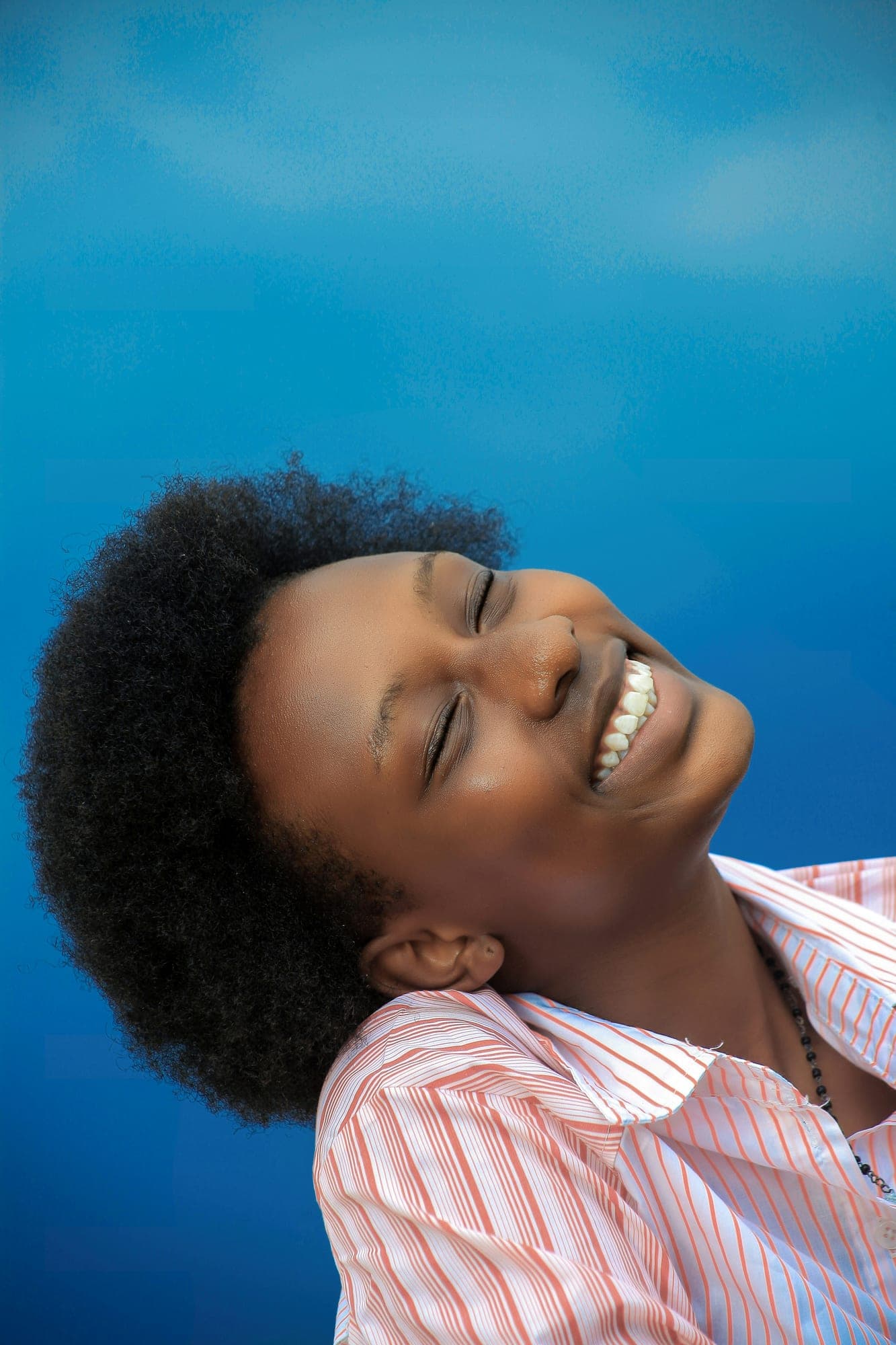 A young person laughs with eyes closed against a vivid blue background