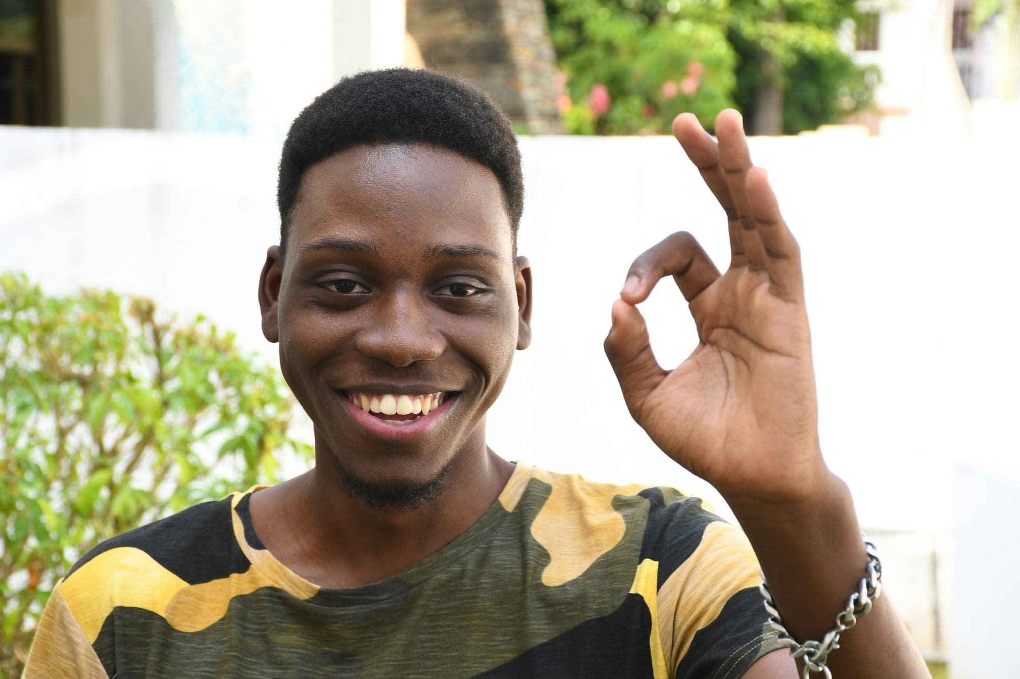 A young man smiles and makes an approving hand gesture outdoors